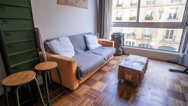 A modern living room with a sofa, two stools, a wooden chest, and a window with a view of buildings. - Modern accommodation, near Parisian attractions (Paris)