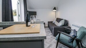 Ett modernt vardagsrum med en soffa, en fåtölj och en matplats med ett bord och en flaska vin.