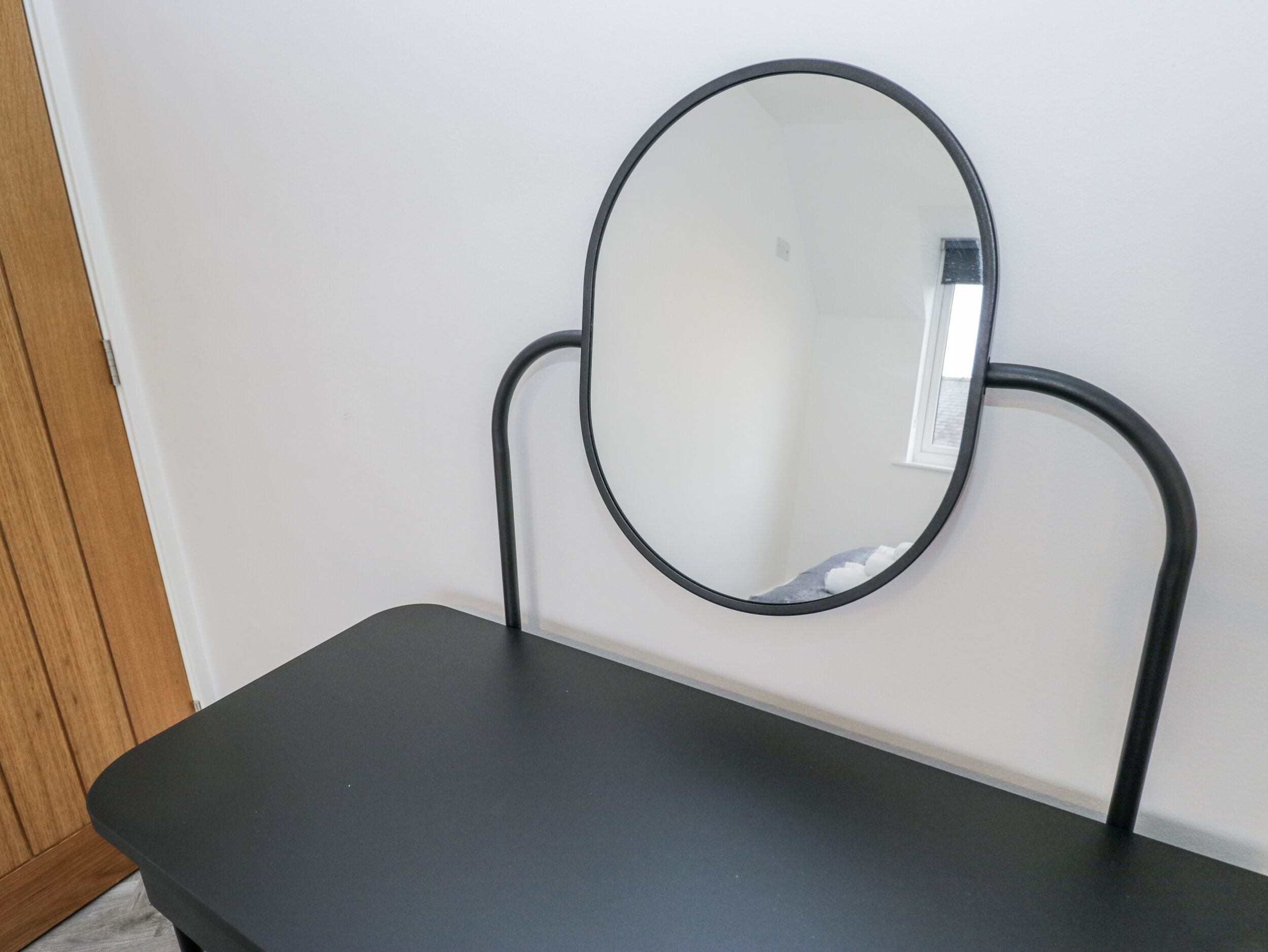A small, dark-colored table with a round mirror mounted on a wall.