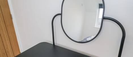 A small, dark-colored table with a round mirror mounted on a wall.