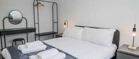 A neatly arranged bedroom with a bed, bedside tables, a desk, a mirror, and a hanging rack.