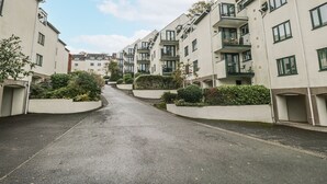 En bostadsgata med moderna hyreshus, en asfalterad väg och välskött grönska.