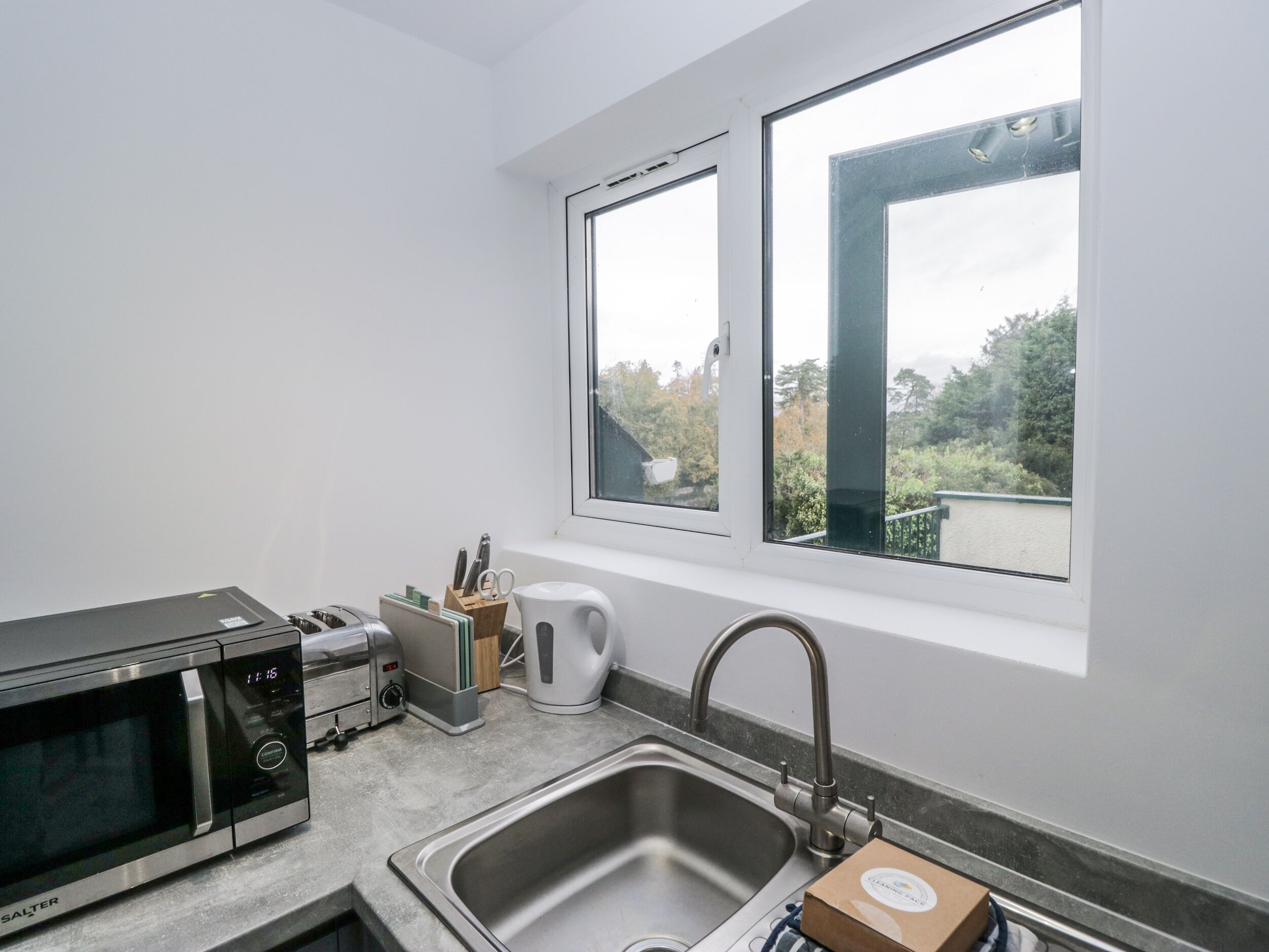 Cucina con microonde, tostapane, lavello e finestra vista sul verde.
