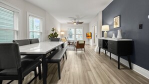 A modern kitchen with a dining area, featuring a large table, chairs, a bench, a ceiling fan, and a dark accent wall. - 3-bedroom apartment-Downtown, Modern, Central, Renovated & Cozy (Buffalo)