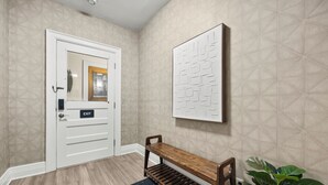 A hallway with a white door marked "EXIT," a wooden bench, a wall-mounted artwork, and a potted plant. - 3-bedroom apartment-Downtown, Modern, Central, Renovated & Cozy (Buffalo)