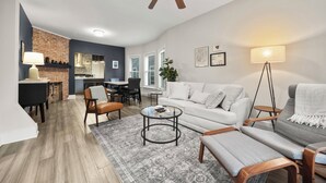 A modern living room with a sofa, armchairs, a coffee table, and a dining area with a brick accent wall. - 3-bedroom apartment-Downtown, Modern, Central, Renovated & Cozy (Buffalo)
