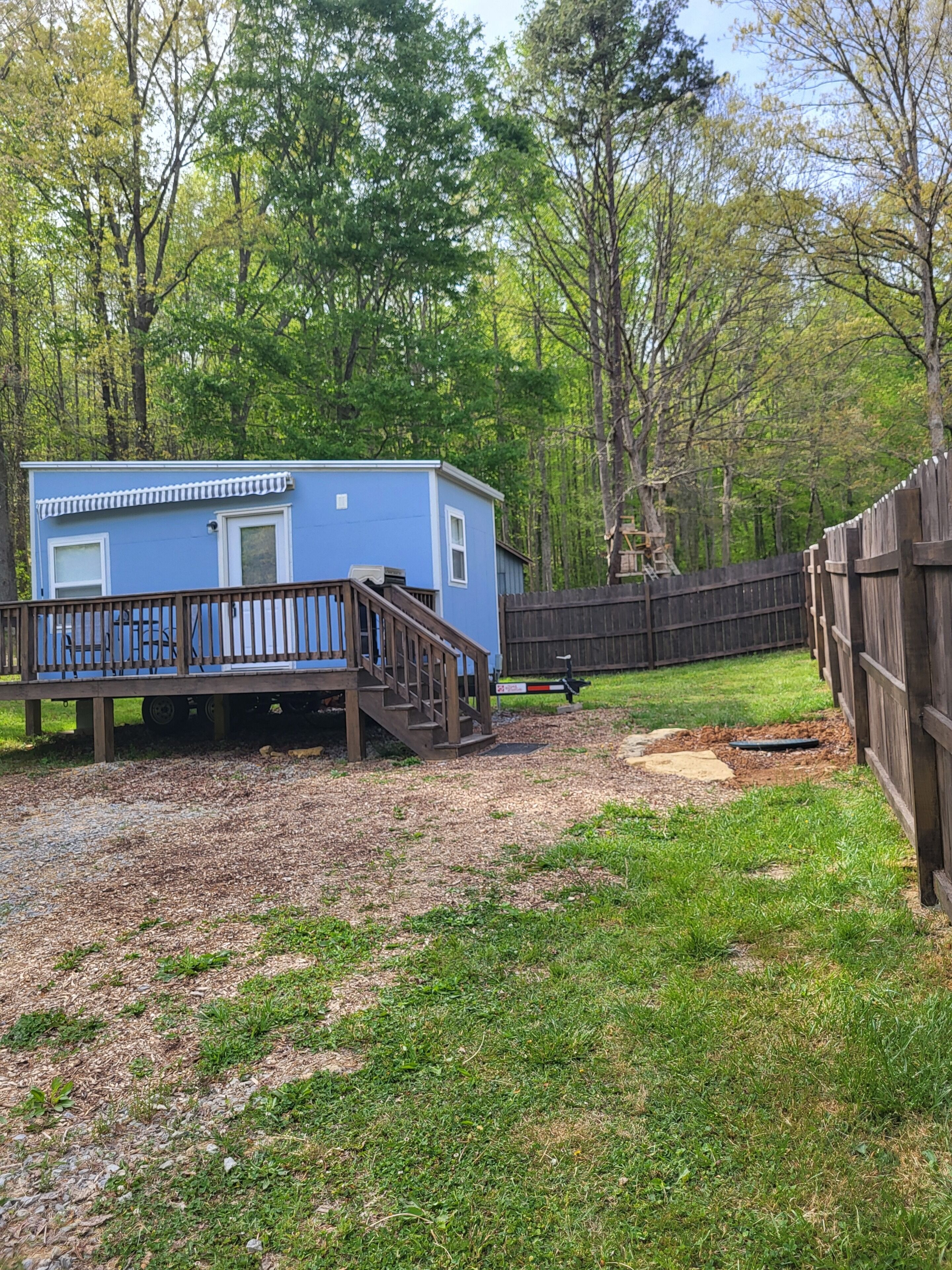 A small blue cabin with a wooden deck and a fenced yard.