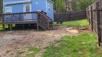 A small blue cabin with a wooden deck and a fenced yard.