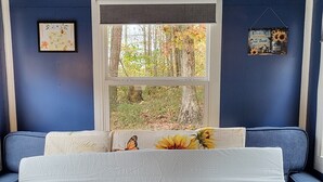 A room with a blue wall, a window with a view of trees, a bed with a white mattress, and a blue sofa.