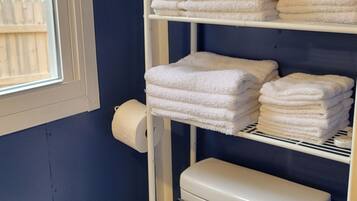 A bathroom with a white toilet, a shelf with folded towels, and a window with blinds.