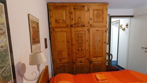 Un dormitorio con un armario grande de madera, una cama con una colcha naranja, una lámpara de pared y un cuadro enmarcado.