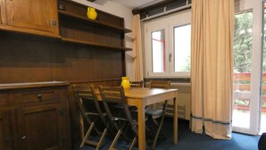 Un comedor con una mesa y sillas de madera, una jarrón amarillo y una ventana con cortinas.