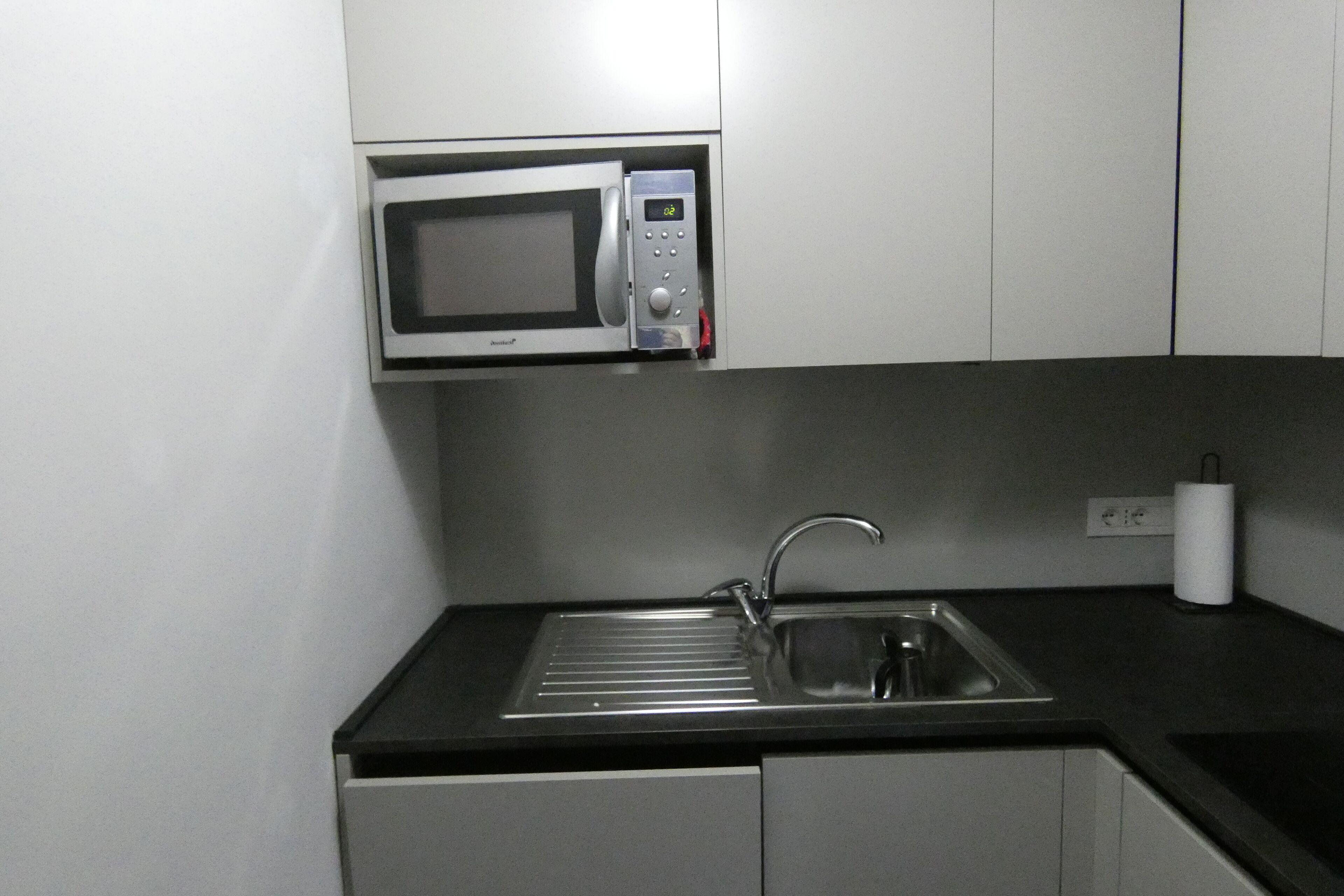 A compact kitchen with a built-in microwave, a stainless steel sink, and a small countertop.