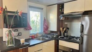Una cocina moderna con un refrigerador de acero inoxidable, un horno integrado y una estufa a gas. Hay una ventana con persianas, un microondas y un florero con flores sobre la encimera.