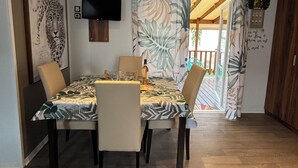 Un área de comedor con una mesa preparada para cuatro, sillas, un televisor montado en la pared y vistas al exterior a través de una puerta.