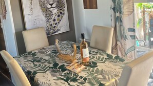 Un comedor con una mesa cubierta por un mantel estampado con hojas, rodeada de sillas. Una botella de vino y un adorno decorativo están sobre la mesa. Un cuadro grande de un leopardo adorna la pared sobre la mesa.