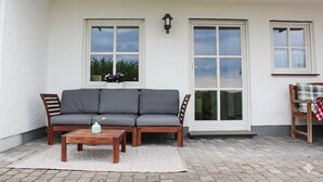 A covered patio with a grey sofa, wooden coffee table, and a small table with a vase. - ✨Charming apartment with panoramic views | Eversberg old town in Hochsauerland (Meschede)