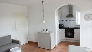 A compact living space with a kitchenette, a sofa, a small cabinet, and a hanging light fixture. - ✨Charming apartment with panoramic views | Eversberg old town in Hochsauerland (Meschede)