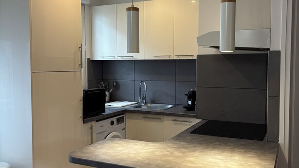 A compact kitchen with white cabinets, a built-in oven, a sink, and a washing machine. - Spacious apartment 15 minutes from Paris (Noisy-le-Sec)