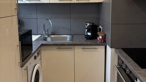 A compact kitchen with a washing machine, a microwave, a sink, and a stove. - Spacious apartment 15 minutes from Paris (Noisy-le-Sec)