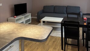 A modern living room with a sofa, a TV, a dining table with chairs, and pendant lights. - Spacious apartment 15 minutes from Paris (Noisy-le-Sec)