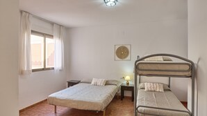 A room with two beds, a window with curtains, a wall-mounted lamp, and a decorative wall piece.