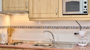 A kitchen with wooden cabinets, a stainless steel microwave, a sink, and a coffee maker.