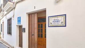 A building with a wooden door, a blue sign with 'AT' and 'CIFEROS' on the wall, and a sign indicating '3' above the door.