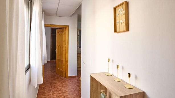 A hallway with a wooden door, a wall-mounted key rack, and a wooden console table with three candle holders.