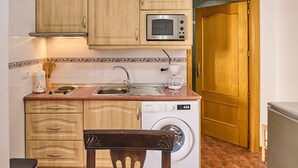A compact kitchen with wooden cabinets, a built-in microwave, a washing machine, and a sink.