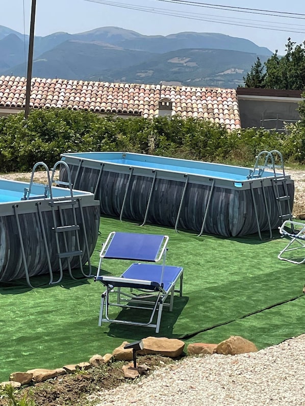 An outdoor swimming pool area with multiple inflatable pools, a sun lounger, and a view of a mountainous landscape. - In Country Luxury Lodges (Camerino)
