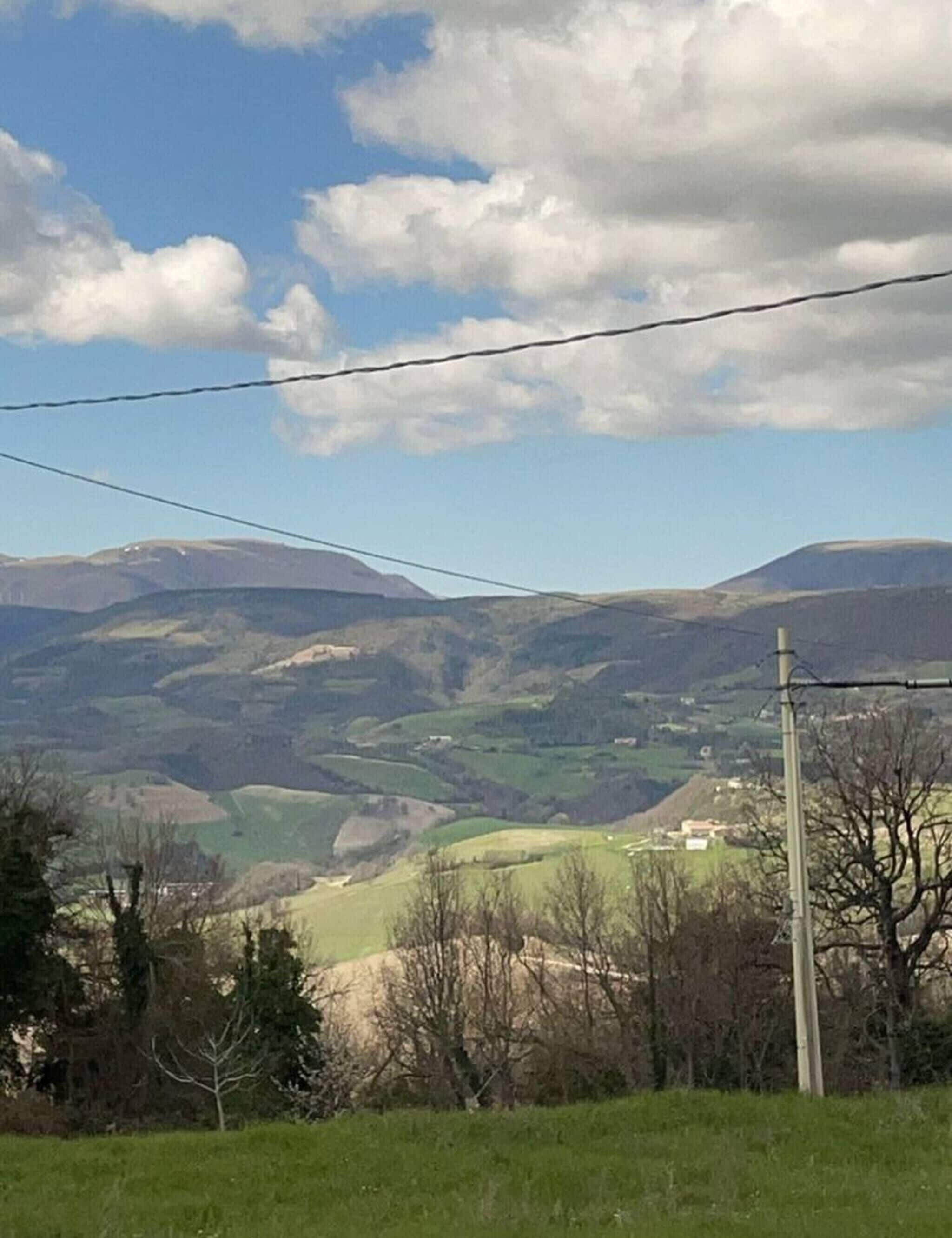 A rural landscape with rolling hills, a clear sky, and a power line in the foreground.