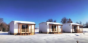 Three small, snow-covered cabins with wooden railings, set in a snowy landscape. - In Country Luxury Lodges (Camerino)