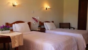 Habitación de hotel con dos camas individuales, una mesita de noche de madera con un teléfono, una pequeña mesa con un jarrón de flores e iluminación en la pared.