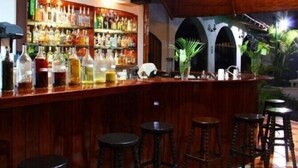 Una zona de bar con una barra de madera, varios taburetes y una estantería llena de licores.
