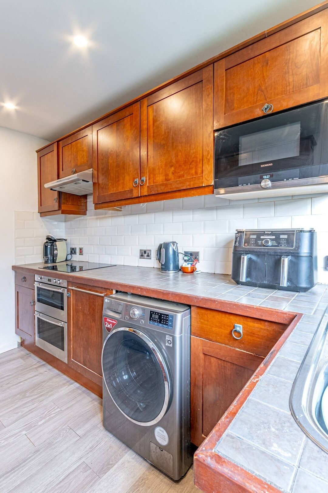 A modern kitchen with wooden cabinets, stainless steel appliances, a built-in oven, a washing machine, and a microwave.