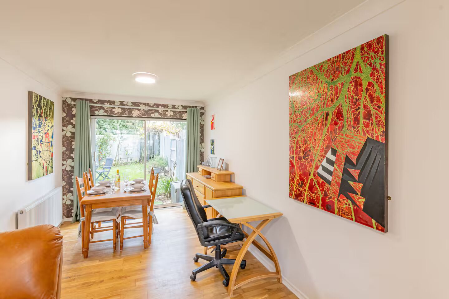 Un comedor con una mesa, sillas y un escritorio con una silla. Hay un cuadro abstracto grande en la pared.