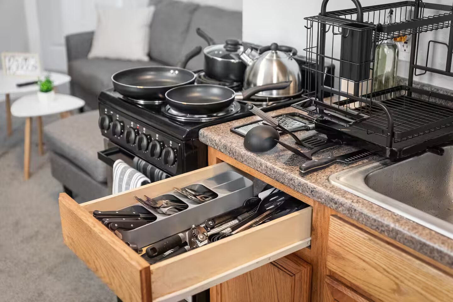 A kitchen with a stove, pots, pans, and a drawer with utensils.