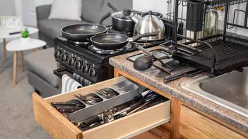 A kitchen with a stove, pots, pans, and a drawer with utensils.