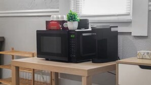 Une cuisine avec un four à micro-ondes posé sur une table en bois, une plante en pot et une machine à café.