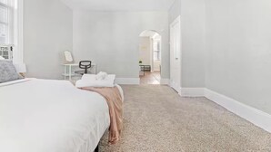 A hotel room with a large bed, a desk, a chair, and a bathroom visible through an archway. - Cute Apt · Little Italy · Fast Wifi · Cozy Bed (Cleveland)