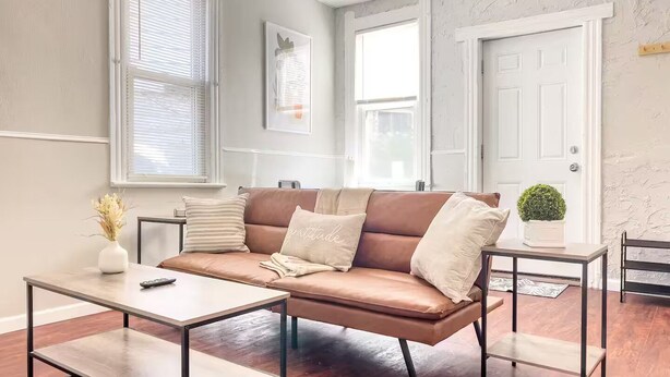 A modern living room with a brown leather sofa, a wooden coffee table, and a small side table with a potted plant. - Cute Apt · Little Italy · Fast Wifi · Cozy Bed (Cleveland)
