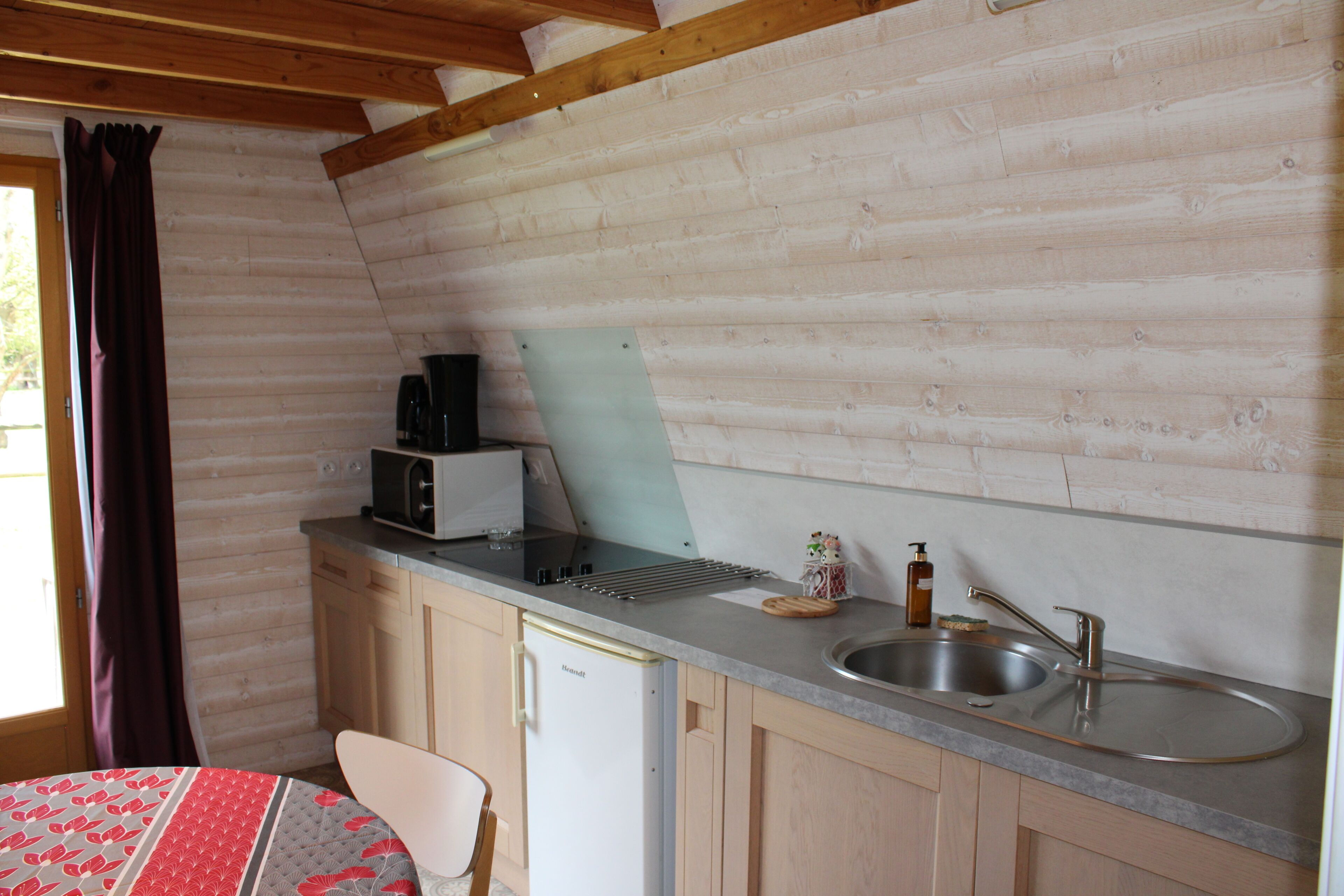 Cocina compacta con paredes de madera, un lavamanos, un microondas y un refrigerador.