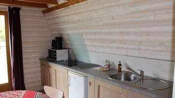 Cocina compacta con paredes de madera, un lavamanos, un microondas y un refrigerador.