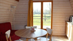 Una cabaña de troncos con una mesa redonda de madera, sillas blancas, un sofá rojo y vistas a un campo cubierto de hierba a través de un ventanal.