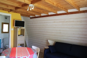 Ein Zimmer mit Holzbalkendecke, einem Bett, einem Fernseher, einem Schreibtisch und einem Stuhl.