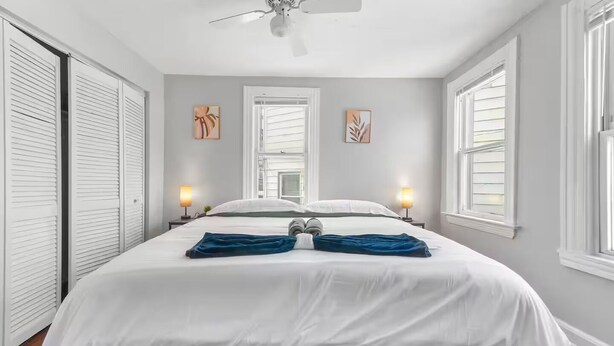 A bedroom with a bed, two bedside lamps, a ceiling fan, and two windows with blinds. - Little Italy · Group Stay · 4 TV's · Pet Friendly (Cleveland)