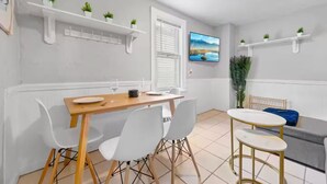 A modern dining area with a wooden table, white chairs, and a TV mounted on the wall. - Little Italy · Group Stay · 4 TV's · Pet Friendly (Cleveland)