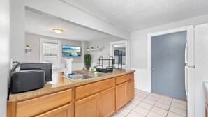 A compact kitchen with a granite countertop, wooden cabinets, a built-in sink, and a refrigerator. - Little Italy · Group Stay · 4 TV's · Pet Friendly (Cleveland)