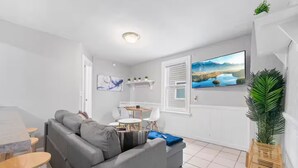 A modern living room with a grey sofa, a small table, and a TV mounted on the wall. - Little Italy · Group Stay · 4 TV's · Pet Friendly (Cleveland)